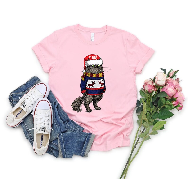 K&ouml;nnte beinhalten: Rosa T-Shirt mit einem Aufdruck eines Katers, der einen Weihnachtsmann-Hut und einen Rentier-Pullover tr&auml;gt. Der Text "My Mode" steht auf dem Hut.