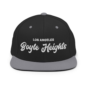 May include: Black and grey baseball cap with white embroidered text that reads "Los Angeles Boyle Heights".