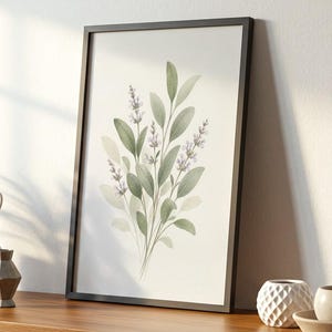 May include: A framed botanical print featuring a watercolor illustration of green leaves and lavender flowers. The artwork is displayed on a white cabinet with a wooden top, alongside decorative items like a potted plant, figurines, and small vases.
