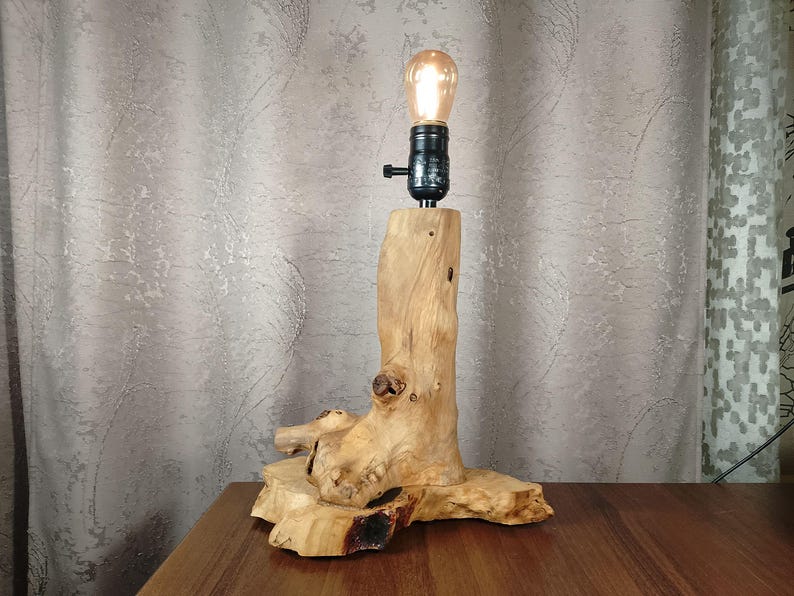 Puede incluir: Una l&aacute;mpara de mesa de madera con una base de madera natural y una bombilla. La base tiene forma de tronco de &aacute;rbol con ramas.