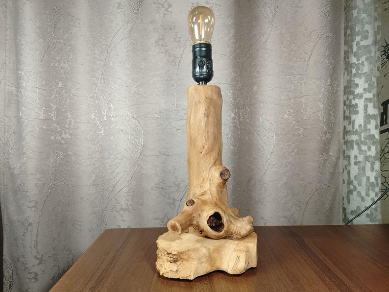 Puede incluir: Una l&aacute;mpara de mesa de madera r&uacute;stica con una base de madera natural y una bombilla simple. La l&aacute;mpara est&aacute; hecha de un trozo de madera a la deriva con una forma natural y org&aacute;nica.