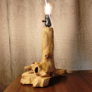 Puede incluir: Una l&aacute;mpara de mesa de madera con una base de madera natural y una bombilla. La l&aacute;mpara est&aacute; sobre una mesa de madera.