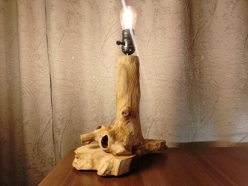 Puede incluir: Una l&aacute;mpara de mesa de madera con una base de madera natural y una bombilla. La l&aacute;mpara est&aacute; sobre una mesa de madera.
