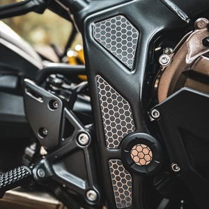 May include: Close-up of a black motorcycle engine with a honeycomb pattern on the side. The engine is made of metal and has a silver finish. The honeycomb pattern is a decorative element that adds a unique touch to the motorcycle.