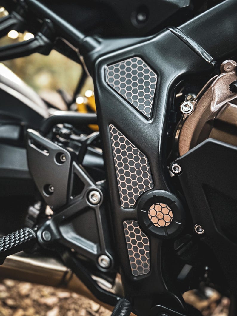 May include: Close-up of a black motorcycle engine with a honeycomb pattern on the side. The engine is made of metal and has a silver finish. The honeycomb pattern is a decorative element that adds a unique touch to the motorcycle.