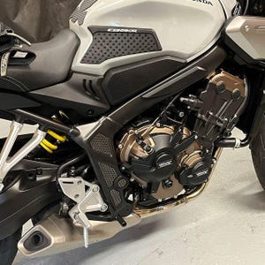 May include: Close-up of a black motorcycle with a gray gas tank and black engine guards. The motorcycle has a black seat and a black exhaust pipe. The gas tank has a black sticker with the word "CB650R" on it.