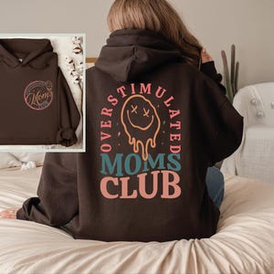a woman sitting on a bed wearing a brown hoodie