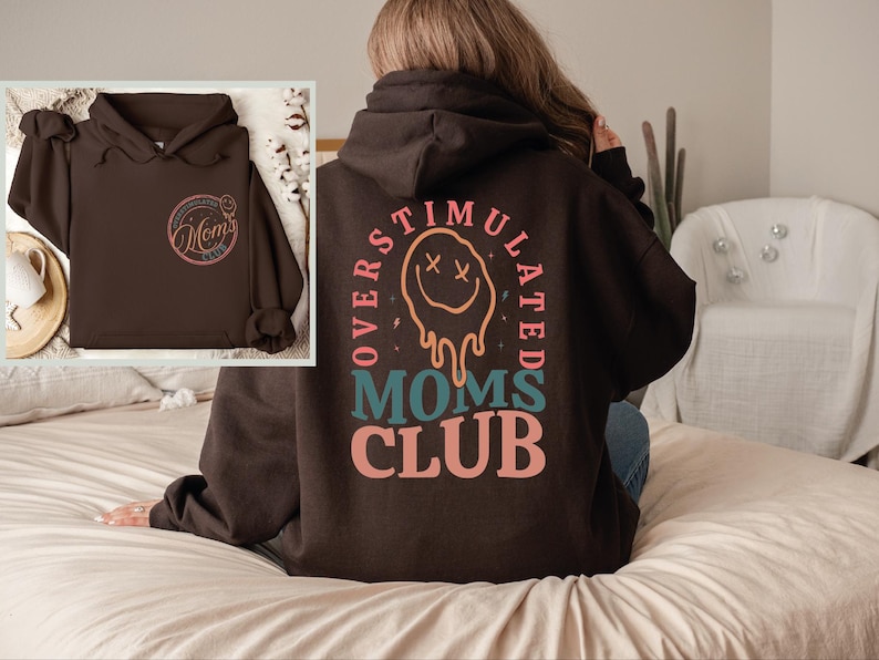 a woman sitting on a bed wearing a brown hoodie