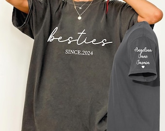 May include: A dark gray oversized t-shirt with the text "besties since.2024" on the front and the names "Angelina, Jane, Jasmin" and a heart on the sleeve.