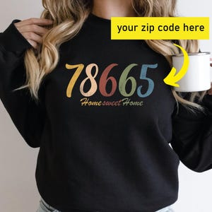 May include: Black sweatshirt with the zip code "78665" in colorful lettering. The words "Home sweet Home" are below the numbers. A yellow box with the text "your zip code here" is in the upper right.