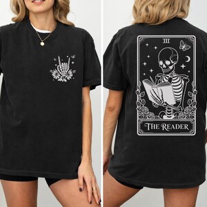 a woman wearing a black t-shirt with a graphic design on the back. The design features a skeleton holding a book, with the text "The Reader" below the skeleton.