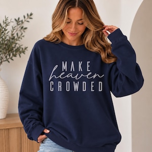 Puede incluir: Una sudadera de manga larga y cuello redondo en color azul marino con el texto "MAKE heaven CROWDED" impreso en gris claro en el pecho. La prenda presenta cuello, puños y dobladillo acanalados, con un diseño de color sólido.