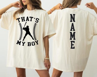 May include: Two white t-shirts with black text and graphics. The front shirt has a baseball player silhouette with the text "That's My Boy". The back shirt has the text "NAME" vertically down the back.