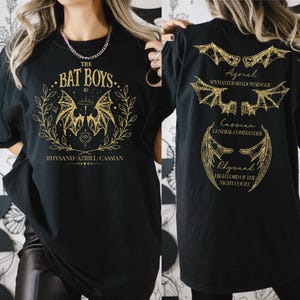 a woman wearing a bat boys t - shirt in front of a wall