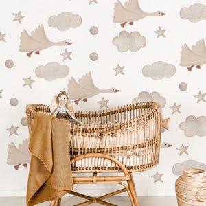 May include: A wicker bassinet with a brown blanket and a stuffed bunny sits in front of a white wall with a repeating pattern of clouds, stars, and geese.