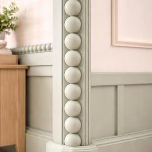 Puede incluir: Una esquina de la habitación con una columna decorada con una fila de grandes esferas esféricas de color claro. La columna está pintada en un verde suave y apagado, y las paredes son de color rosa pálido.