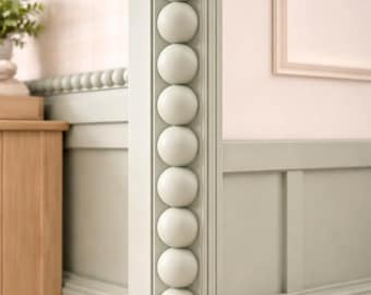 May include: A sage green architectural column featuring a vertical row of stacked spherical beads. The column is integrated into a paneled wall section with a matching sage green finish, showcasing a smooth, matte texture and clean lines.