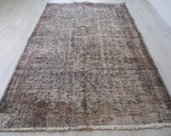 May include: A vintage rug with a faded floral pattern in shades of brown and beige. The rug has a frayed edge and a distressed look.