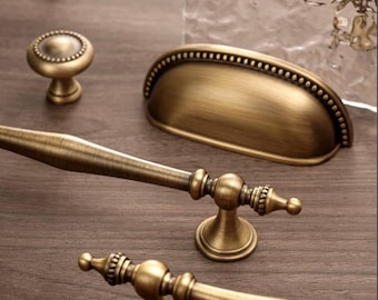 May include: An assortment of antique brass cabinet hardware, including drawer pulls, knobs, and a cup pull. The hardware features ornate detailing and a warm, aged finish, perfect for vintage-style furniture.