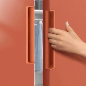 Pode incluir: Close-up de uma porta de armário cor de coral com uma puxador embutido. A porta está parcialmente aberta, revelando um vislumbre do interior. O puxador tem a mesma cor da porta. O armário parece fazer parte de uma unidade de armazenamento maior.