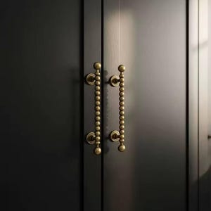 May include: Close-up of a black cabinet door with two brass-colored pull handles. Each handle is composed of a series of small, round beads strung together, with a larger ball at each end. The handles are mounted on circular backplates.
