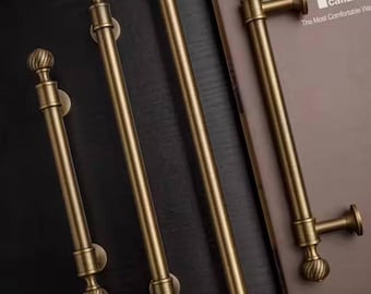 May include: Four antique brass door handles with a decorative ball finial design. The handles are in varying lengths and are mounted on a dark surface. The image also shows a book with the text "caliaitalia" and "The Most Comfortable Way".