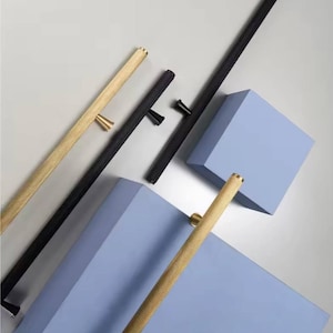 Op de afbeelding: Een assortiment gouden en zwarte kastgrepen en handgrepen. De gouden handgrepen hebben een textuur, geribbeld ontwerp. De zwarte handgrepen zijn glad. De hardware is diagonaal geplaatst tegen een lichtgrijze en blauwe achtergrond.