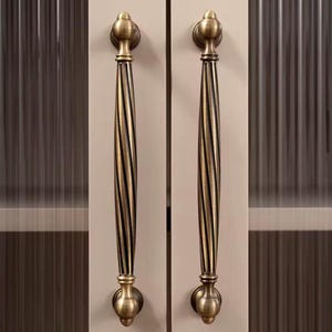 Peut inclure: Deux poignées de porte d'armoire de style antique. Les poignées sont en métal de couleur laiton avec un design torsadé et rainuré. Chaque poignée a un dessus et un bas arrondis, et elles sont montées sur une porte d'armoire de couleur claire.