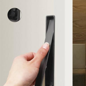 May include: A dark grey cabinet pull is shown open, revealing the interior. The pull is mounted on a white cabinet door. A matching circular pull is also visible. The background is blurred.