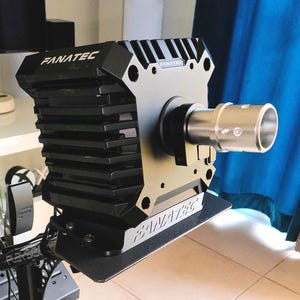 Op de afbeelding: Een zwarte en zilveren Fanatec race-stuurwielbasis. De basis heeft een geribbeld ontwerp aan de zijkanten en het Fanatec-logo is zichtbaar aan de boven- en voorkant. Een zilveren cilindrisch onderdeel strekt zich uit vanaf de basis.