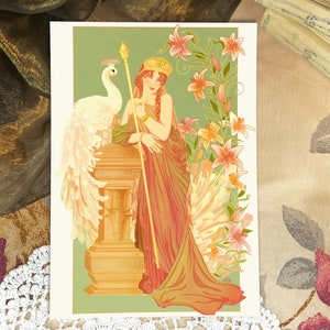 Peut inclure: Une femme vêtue d'une robe fluide orange et verte se tient avec un paon blanc à ses côtés. Elle tient un bâton doré et porte une couronne de feuilles d'or. L'arrière-plan est un motif floral vert et orange.