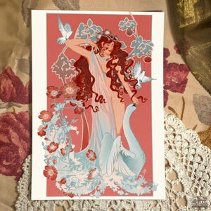 Puede incluir: Una mujer con el pelo largo y rojo y un vestido blanco se encuentra con un cisne en un entorno floral. El fondo es de color rosa con flores y hojas blancas. La mujer lleva una corona de flores y tiene una expresión delicada en su rostro.