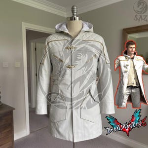 May include: A white hooded coat featuring a quilted shoulder pattern, gold-toned toggle closures, and zippered chest pockets. The coat is displayed on a mannequin, with an inset image showing a person wearing the same coat with a textured sweater.