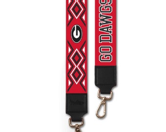 Puede incluir: Correa de bolso con estampado rojo y blanco con el texto "GO DAWGS" en blanco y negro. La correa presenta un extremo de cuero negro con cierres metálicos dorados y el logotipo de la Universidad de Georgia.