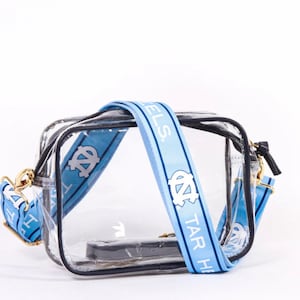 May include: Clear plastic crossbody bag with a blue and white adjustable strap that says "Tar Heels" and features the University of North Carolina logo.
