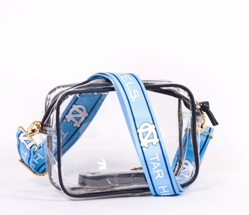 May include: Clear plastic crossbody bag with a blue and white adjustable strap that says "Tar Heels" and features the University of North Carolina logo.