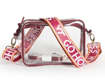 May include: A clear rectangular crossbody bag with maroon trim and a detachable maroon strap featuring the white text VT GO HOKIES. The bag includes gold-tone metal hardware clips and a separate smaller maroon strap wrapped in clear plastic packaging.