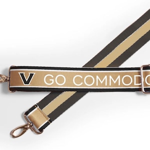 May include: A black and gold adjustable strap with a white stripe and the text "V GO COMMODORE" printed on it.