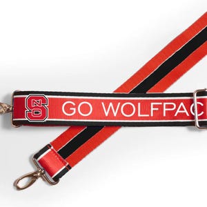 K&ouml;nnte beinhalten: Verstellbarer Gurt in Rot und Schwarz mit einem wei&szlig;en Streifen und dem Text "GO WOLFPACK" sowie einem rot-schwarzen NC State-Logo.