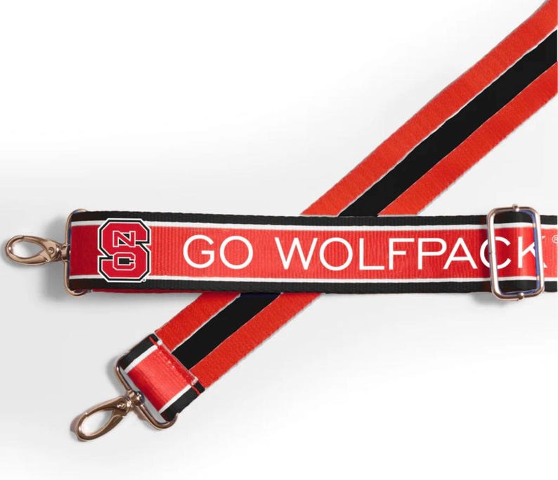 K&ouml;nnte beinhalten: Verstellbarer Gurt in Rot und Schwarz mit einem wei&szlig;en Streifen und dem Text "GO WOLFPACK" sowie einem rot-schwarzen NC State-Logo.