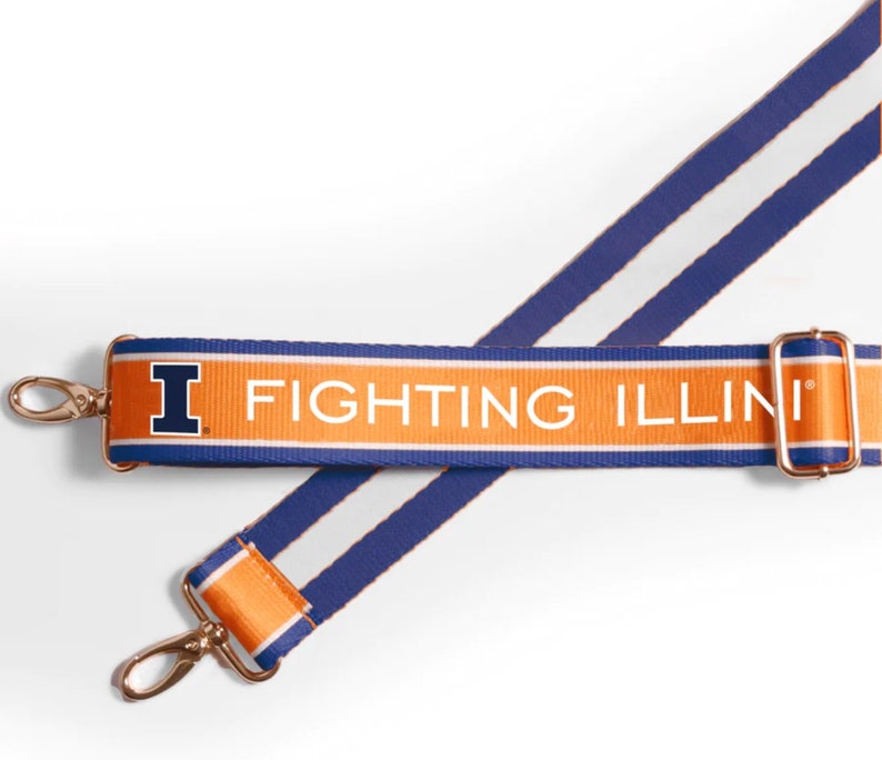 May include: Orange and blue shoulder bag strap with the text "FIGHTING ILLINI". The strap has gold-colored metal clasps and a blue and white striped pattern. The University of Illinois logo is visible.
