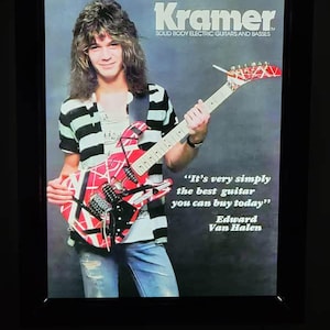 May include: Framed Kramer guitar advertisement featuring Edward Van Halen. The image shows Van Halen holding a red, white, and black electric guitar. The text reads "It's very simply the best guitar you can buy today" and "Edward Van Halen."