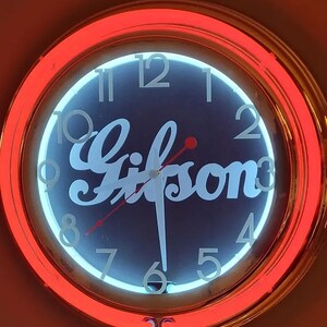Op de afbeelding: Een rode neonklok met een gouden frame en een blauwe wijzerplaat. De klok heeft witte cijfers en een witte inscriptie met de tekst "Gifson".