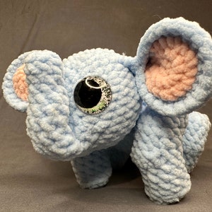 May include: A crocheted blue elephant stuffed animal with pink ears and a black eye.
