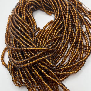 May include: A bundle of small, amber-colored glass beads. The beads are strung together, creating a textured, layered appearance. The beads are a warm, translucent brown color, and are likely used for jewelry making or other crafts.