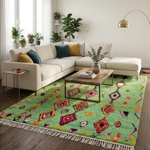 Peut inclure: Salon avec un canapé d'angle crème et des coussins colorés. Un tapis vert vif avec des motifs géométriques et une bordure à franges est posé sous une table basse en bois. Des plantes en pot et un lampadaire doré complètent la pièce.