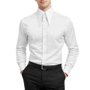 May include: A white dress shirt with a distinctive, tall, pointed collar. The long-sleeved shirt has a button-down front and is paired with black pants and a black belt. The shirt is made of a smooth, likely cotton or a cotton blend fabric.