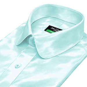 May include: A light blue dress shirt with a rounded collar and buttoned front. The shirt is made of a shiny, satin-like material. A black tag with the text "John Cloth London" and the word "Green" is visible.