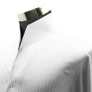 Puede incluir: Camisa blanca de vestir con cuello mandarín y rayas verticales. La camisa tiene un cierre de botón único en el cuello.