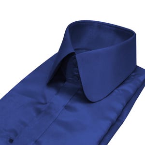 Puede incluir: Camisa azul real doblada, con cuello alto y redondeado. La camisa tiene una botonadura y está hecha de una tela lisa, posiblemente satinada. El cuello es el punto central, con un diseño clásico y formal.